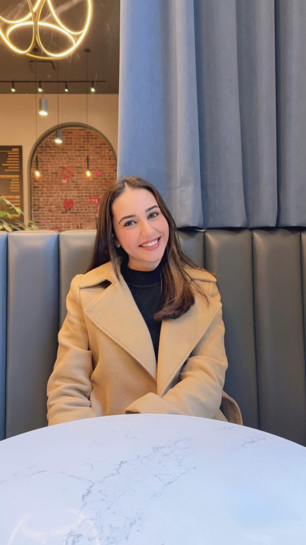 Simran seated in a café in a camel coat.
